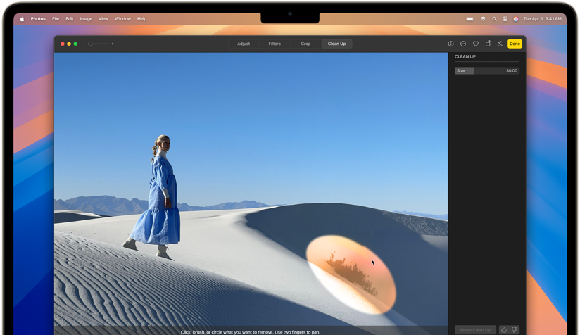 In an open photo in the Photos app on MacBook Air, a person is standing on a desert dune and a small distracting object is highlighted for removal by the Apple Intelligence Clean Up tool