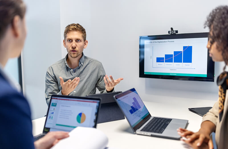 Business team discusses a project in a startup office boardroom, sharing ideas, documents, and laptop screens.