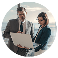 Two business professionals standing with laptop computer in open office