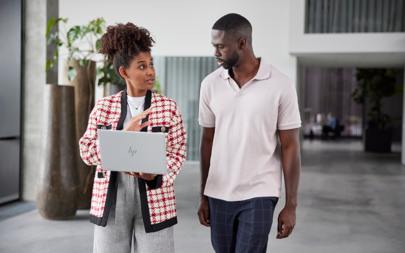 man and woman walking beside one another, the woman is carrying a laptop