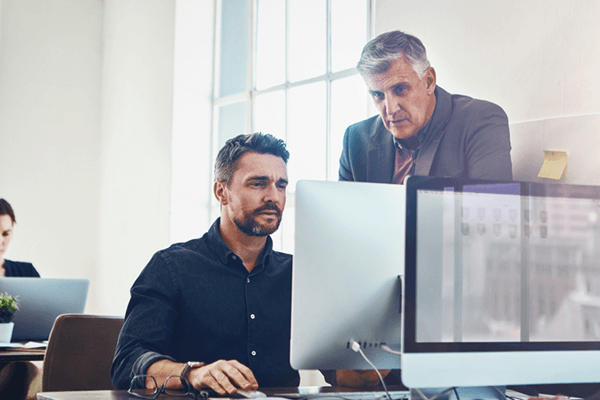 Project manager looks over shoulder at man on desktop overseeing software integration