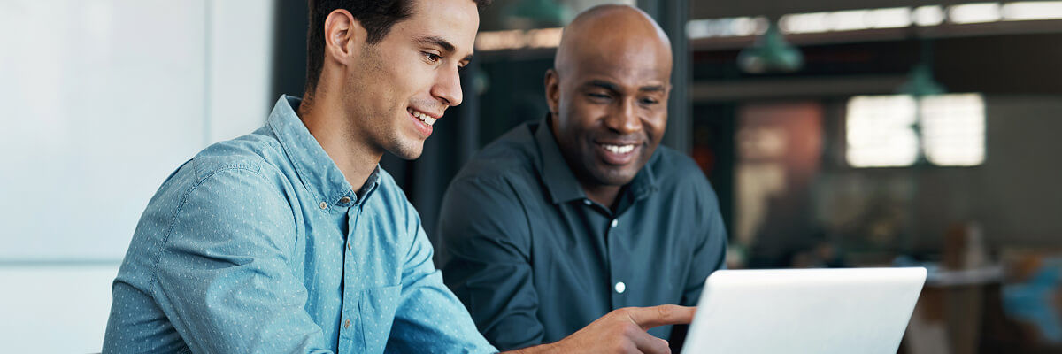 Diverse professionals collaborate on a laptop using Google Workspace in a sunlit, modern open-plan office.