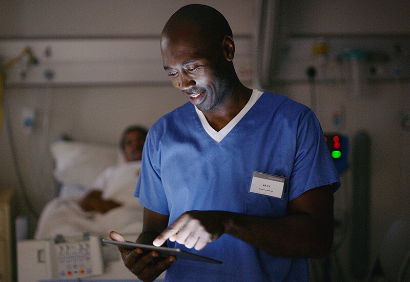 Healthcare provider working in patient room with technology device in hand