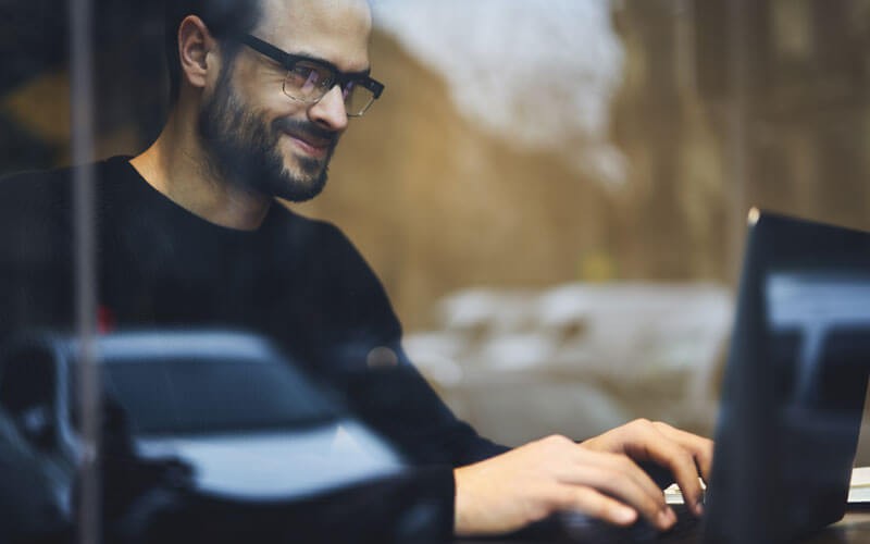 Smiling man reading report on laptop computer