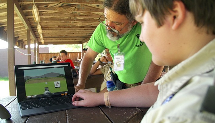 Camp instructor helping Boy Scout with hunting game on notebook computer