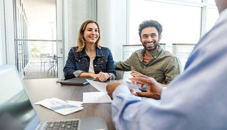 Drive IT modernization through cloud transformation to empower both internal teams and next-gen customers. Smiling couple talks with a credit union banker