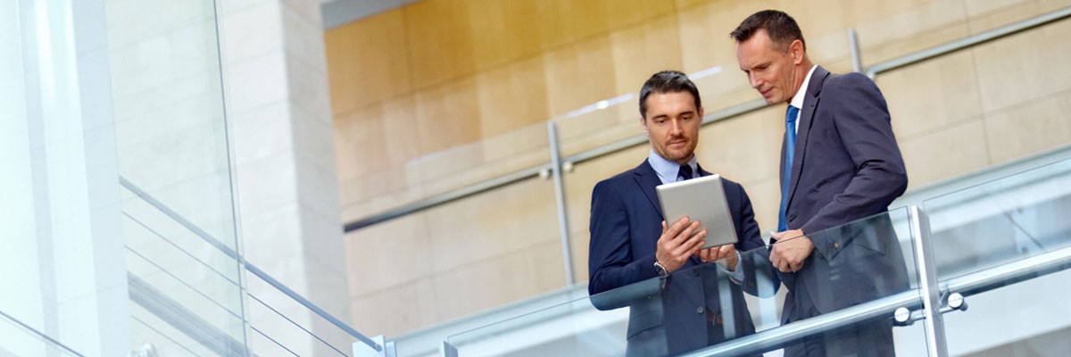 Two businessmen look at tablet device in open office space