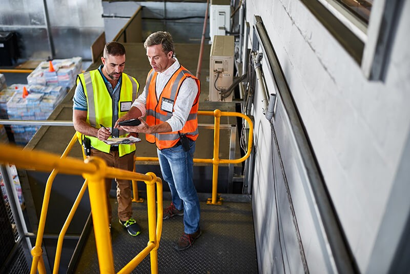 Two men on tablet device in manufacturing facility