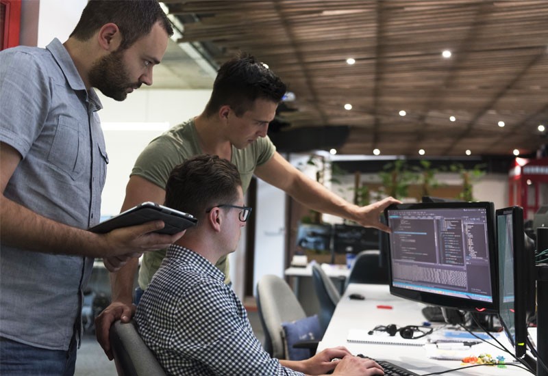 Three male workers collaborating over workstation device 