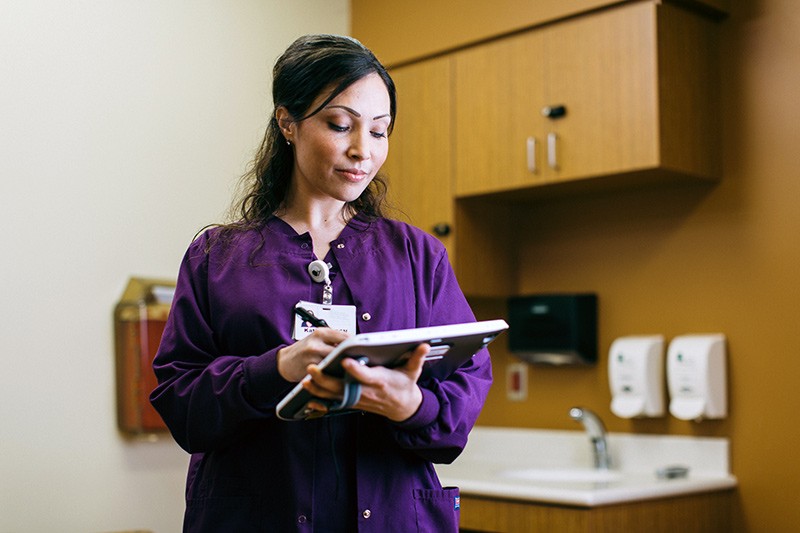 Streamline administrative workflow. Nurse on mobile device looking at patient data.