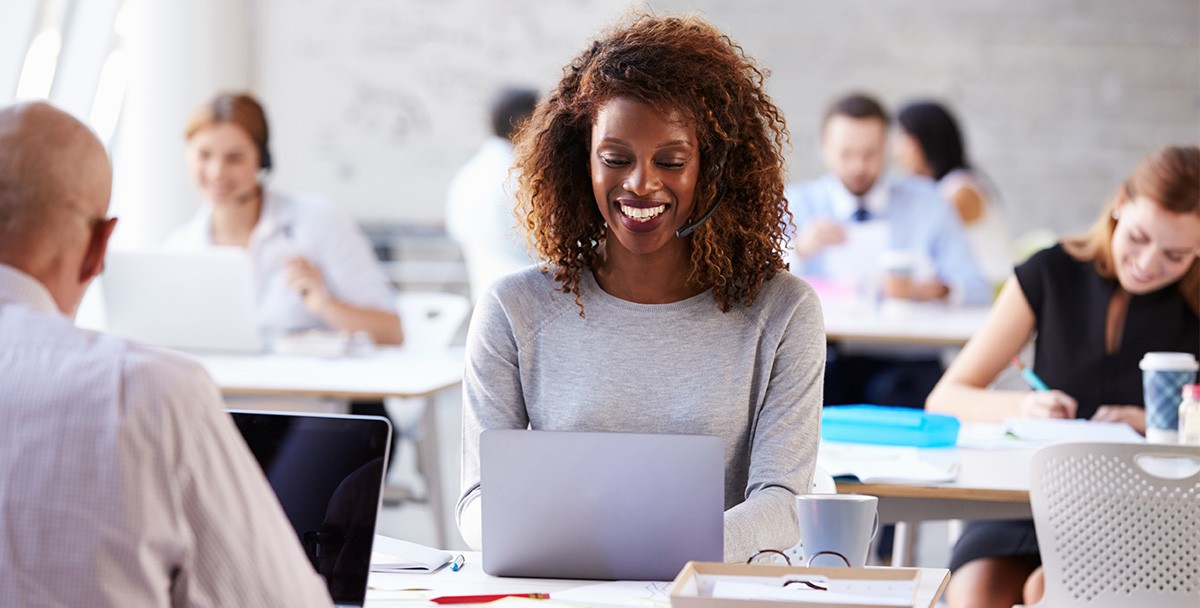 Female worker at contact center appears to be smiling while typing on computer laptop