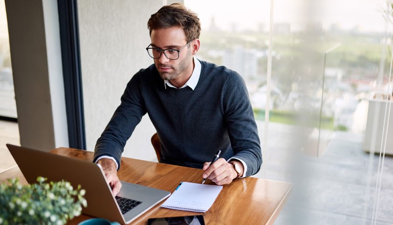 Businessman watching webinar on laptop computer while taking notes