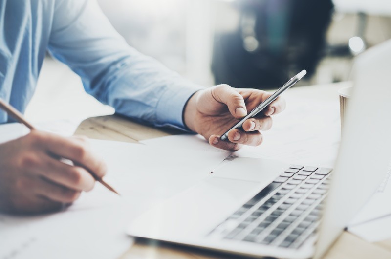 Business man looking at phone while using laptop.