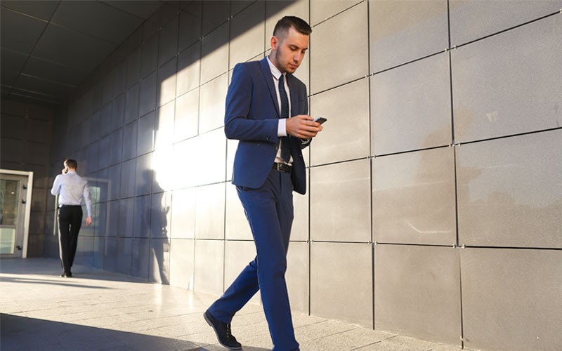 Business man walking outside while texting on mobile phone