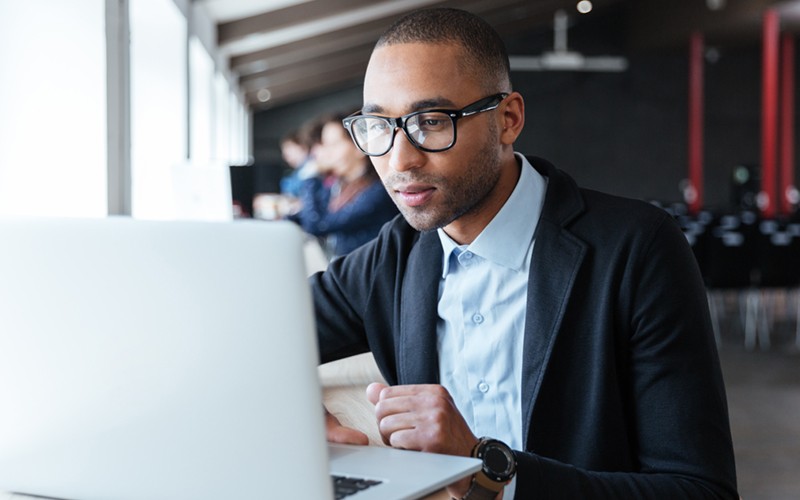 Businessman in glasses on laptop computer in open office