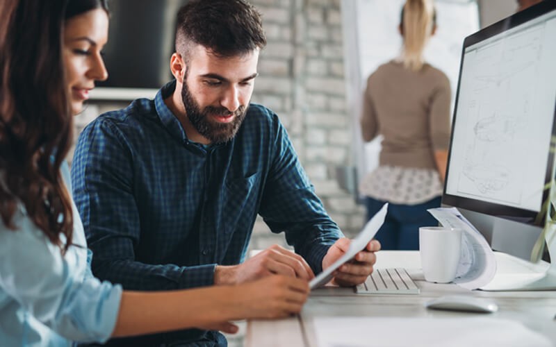 Two business professionals looking over documents in front of desktop computer